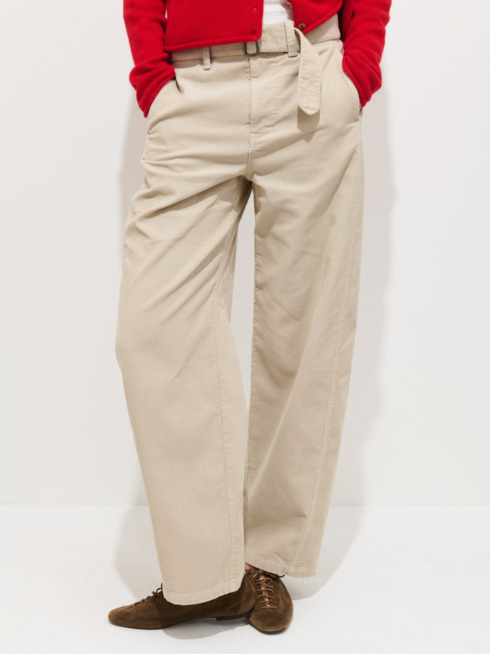 Someone wearing the 9th Street Pant In Fine Wale Cord from Alex Mill, a red top, and brown lace-up shoes stands with hands in pockets against a plain white background.