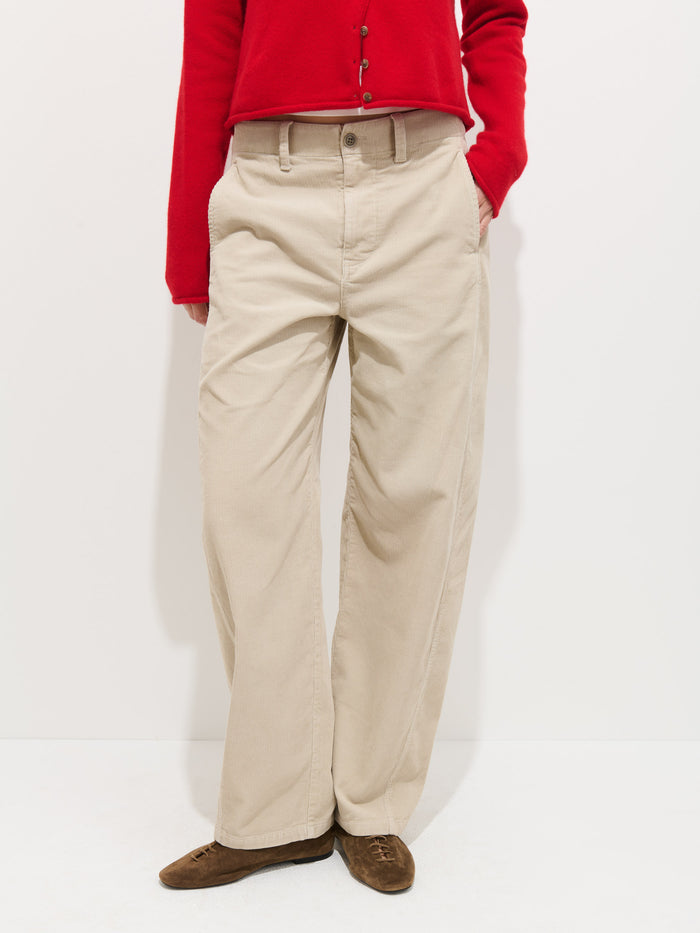 Someone wearing the 9th Street Pant In Fine Wale Cord (beige, barrel shape), a red buttoned long-sleeve top, and brown shoes stands against a plain white background.