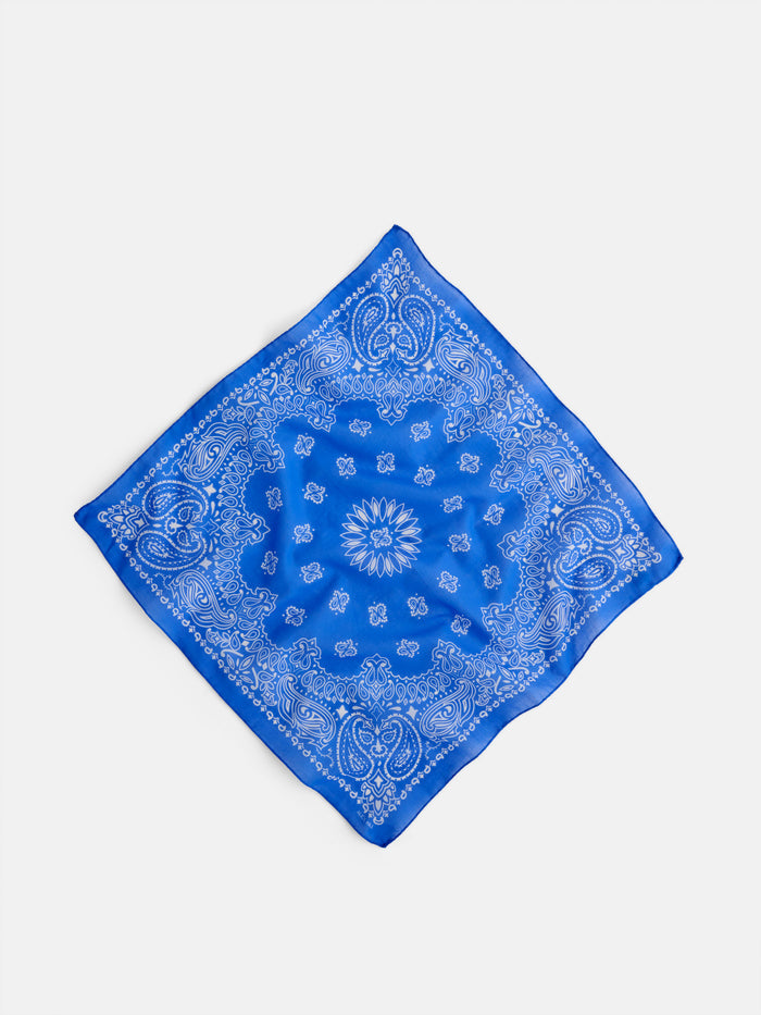 The Bandana in Cotton Voile, featuring a blue hue with a white paisley pattern and made from soft cotton voile, lies flat on a white background, positioned diagonally like a diamond.