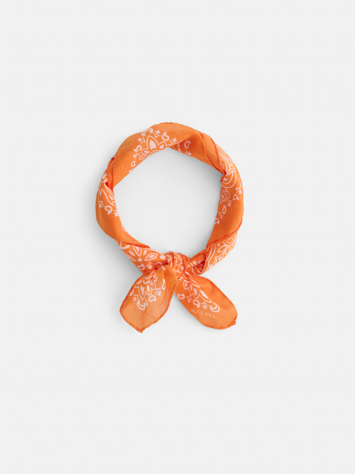 The Bandana in Cotton Voile features an orange vintage design with white paisley patterns, crafted from soft cotton voile and neatly tied in a loop with a small knot, displayed on a plain white background.