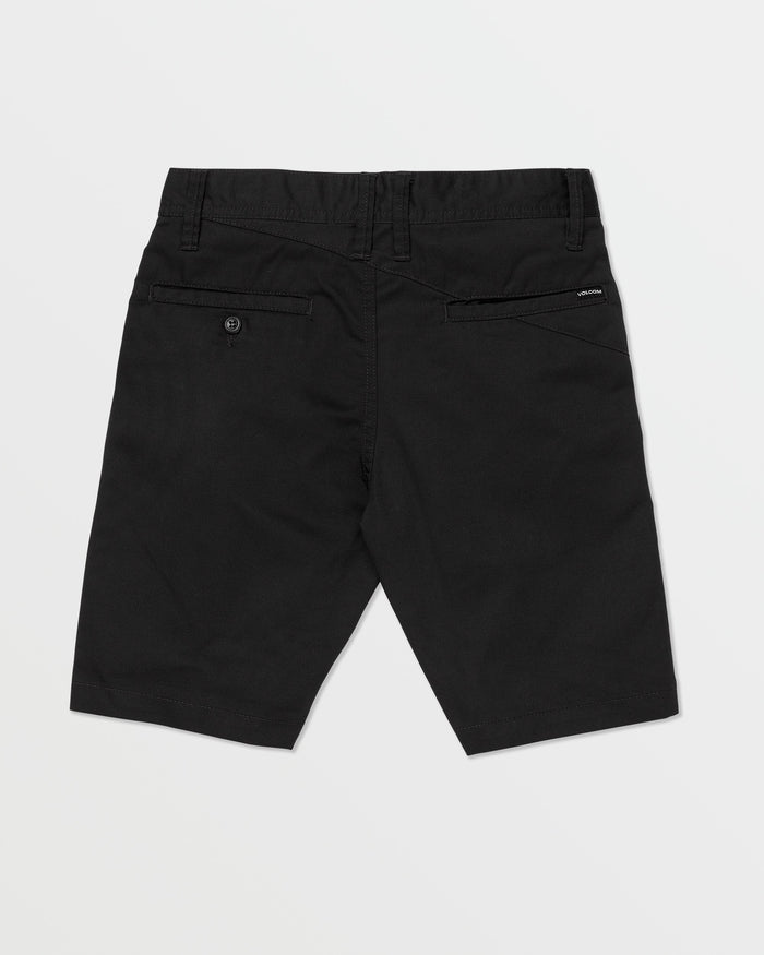 The Volcom Kids' Frickin Chino Shorts 16" are black, knee-length, shown from the back with a modern fit, belt loops, two rear pockets (one buttoned), and a black Volcom label above the right pocket. Shorts are laid flat on a white background.