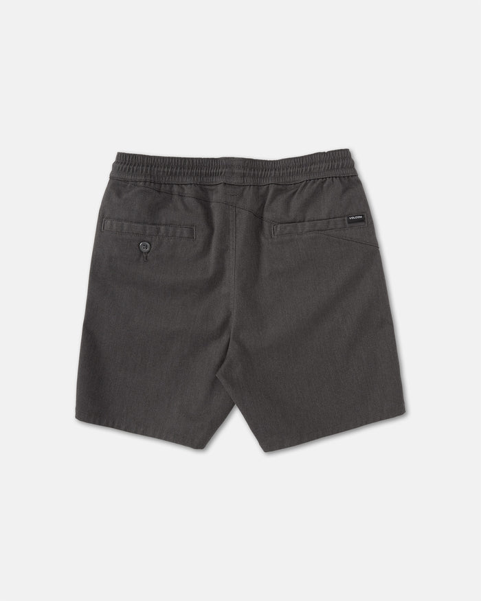 Back view of Volcom Kids' Big Boys' Frickin Elastic Waist Shorts in dark gray, featuring two back pockets (one with button) and a black brand tag above the right pocket. Made from recycled poly-cotton, shorts shown laid flat on a light surface.