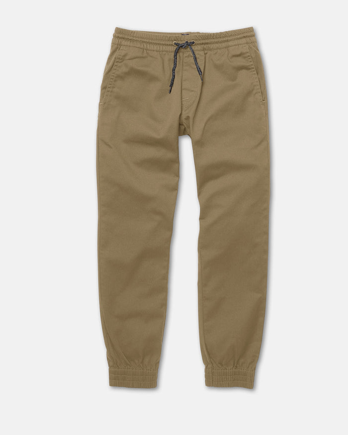 Volcom Kids' Big Boys Frickin Slim Joggers in khaki, made with recycled fibers. Feature an elastic waistband, black drawstring, side pockets, and elastic cuffs at the ankles. Laid flat on a white background.