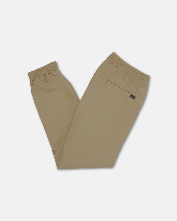 Volcom Kids' Big Boys Frickin Slim Joggers in beige, featuring an elastic waistband, cuffs, and a single back pocket, are crafted from recycled fibers and shown folded with the back side visible on a white background.