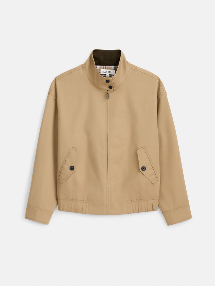 The Brighton Zip Jacket in Twill Gabardine is a tan zip-up jacket made from Italian Gabardine Olmetex, featuring a high collar, buttoned flap pockets, and elastic detailing at the hem. Its water-repellent fabric combines style with practicality, displayed on a white background.