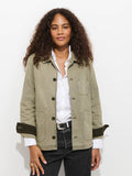 A person with curly hair wears the Britt Work Jacket In Herringbone, which features a corduroy collar, over a white button-up shirt and dark jeans, standing against a white background with a relaxed expression.