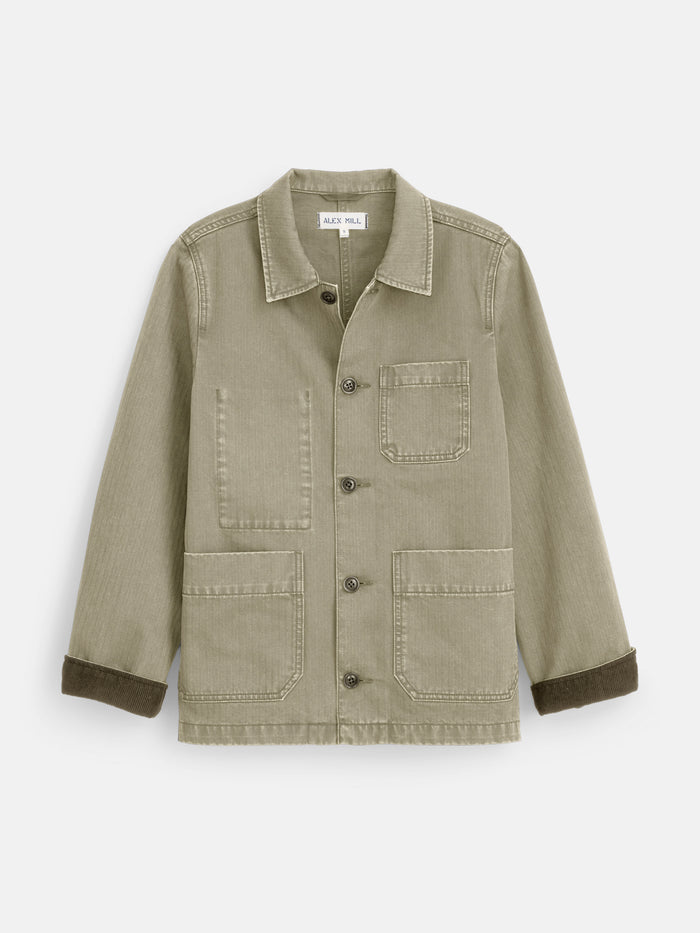 The Britt Work Jacket in Herringbone features a light olive green shade, corduroy collar, button front, three pockets, and turned-up cuffs with darker brown lining—a workwear-inspired classic for fans of timeless utility jackets.