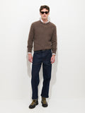 A man wearing sunglasses, a brown sweater layered over a white shirt, Buckle Back Straight Leg Jeans inspired by 1940s workwear in dark blue, and black lace-up boots stands against a plain white background.