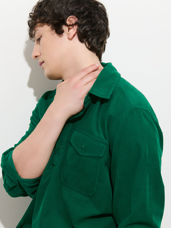 Wearing the Carter Popover In Fine Wale Corduroy—a green, 100% cotton, lightweight shirt—a person touches their neck and gazes to the side against a plain white background.