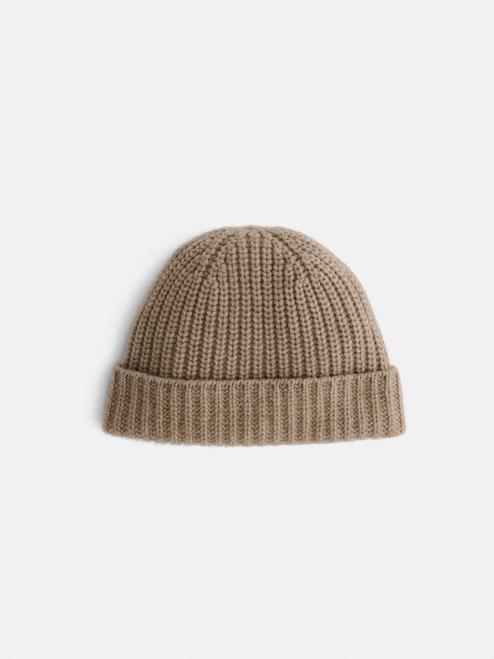 The Cashmere Beanie, featuring a beige ribbed knit design and a folded cuff, is displayed on a plain white background. This soft hat combines warmth with timeless style.