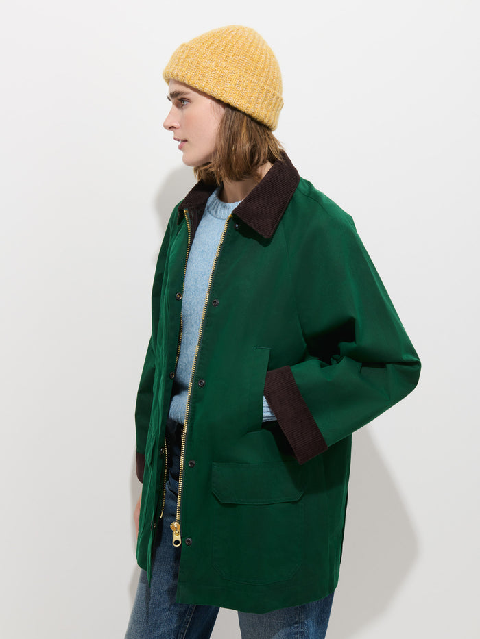 A person wearing a Cashmere Marled Beanie in yellow, a green jacket with a brown collar, a light blue sweater, and jeans stands against a plain white background.
