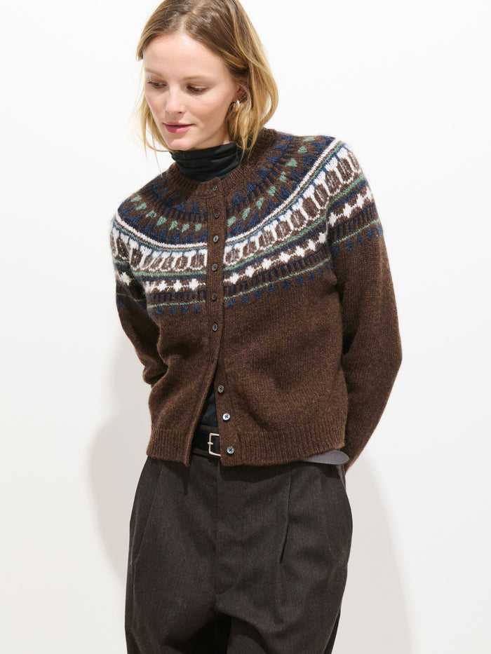 Wearing the Charolette Fairisle Sweater in Wool, a person stands against a plain white background in dark high-waisted trousers, looking down with a slight smile.