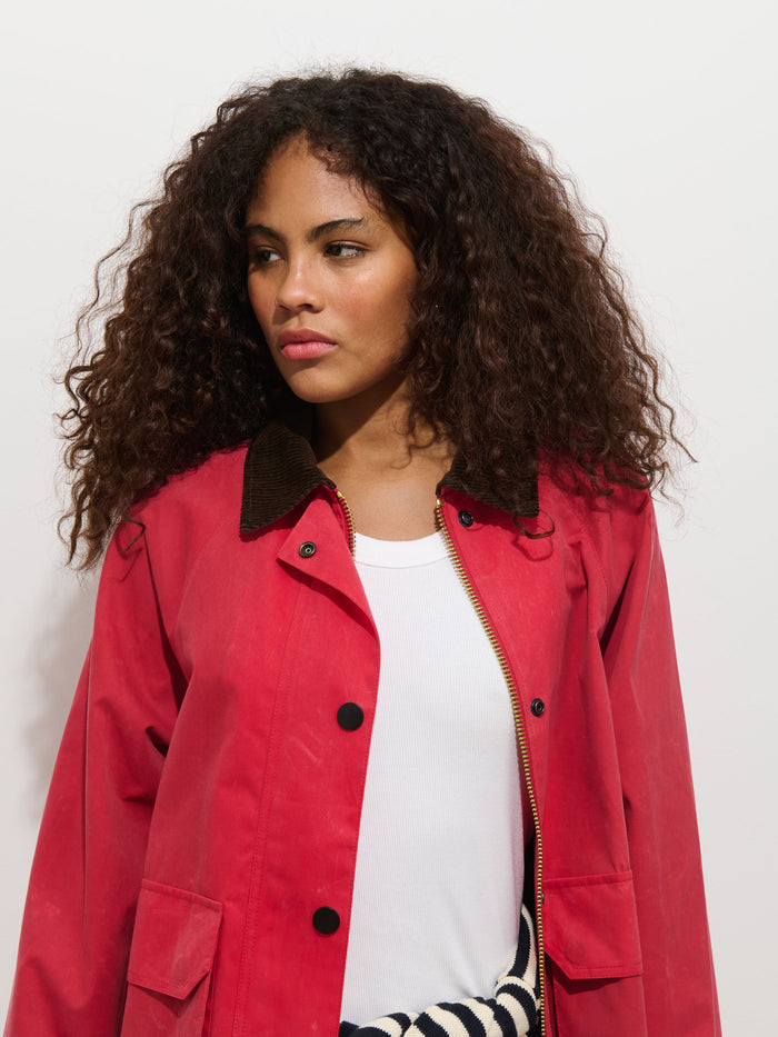 A woman with curly brown hair wears the Chiltern Cropped Jacket in Waxed Canvas over a white top, standing against a plain white background and looking to her left with a neutral expression.