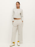 A woman stands against a white background wearing a light gray cotton double jersey long-sleeve buttoned top and matching Coco Sport Pant, paired with yellow socks, white sneakers, and her hands in her pockets for an effortless designer look.