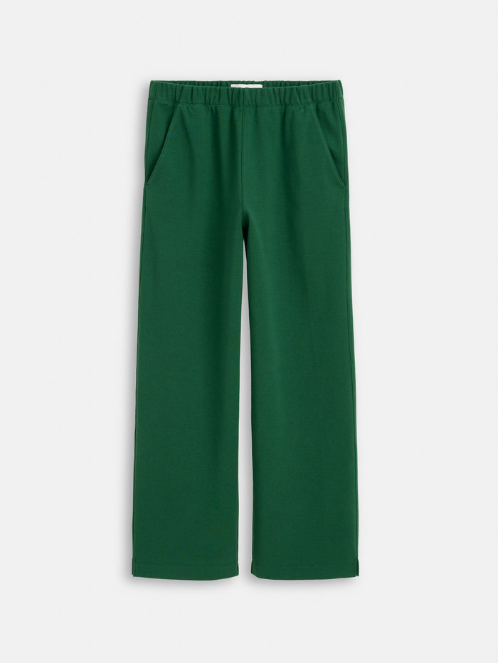 The Coco Sport Pant in dark green is crafted from stretch cotton jersey with a wide-leg fit, elastic waistband, and side pockets, shown against a plain white background.