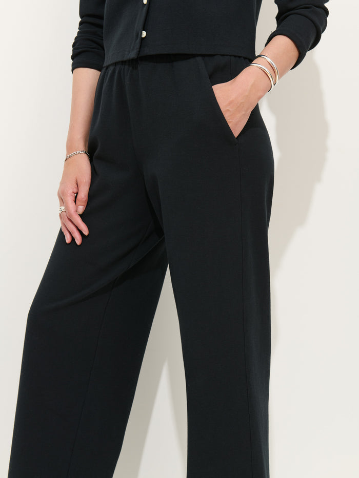 Wearing Coco Sport Pant and a black stretch cotton jersey long-sleeve top, the person stands with one hand in their pocket, rings and bracelets visible. The cropped image highlights women’s designer style from the shoulders down.