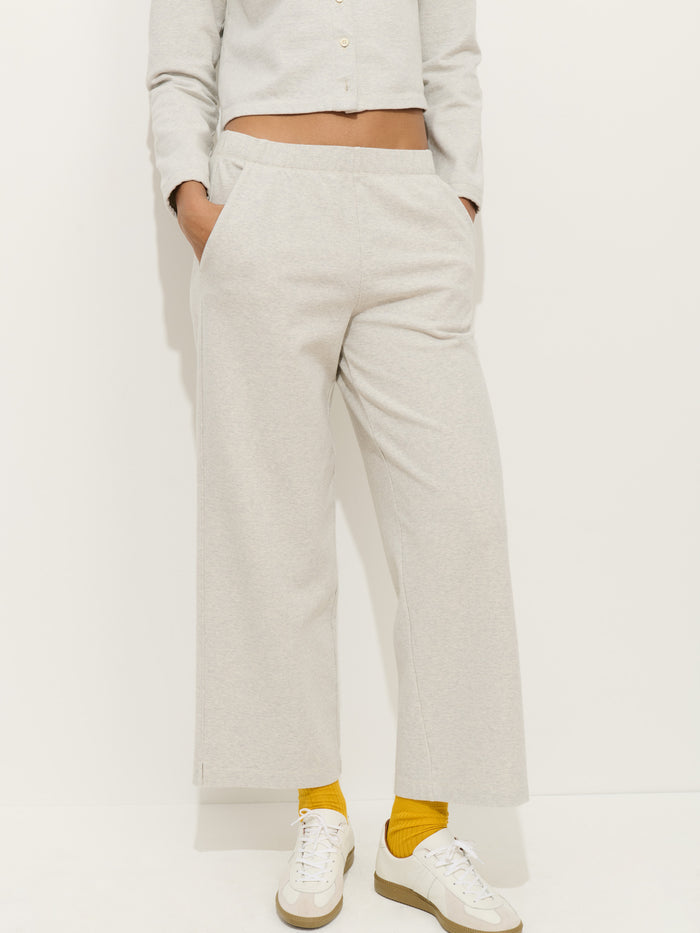 Person modeling light gray Coco Sport Pant in cotton double jersey with a matching cropped long-sleeve top, yellow socks, and white sneakers, standing against a plain white background. The face is not visible. A chic women's designer look.