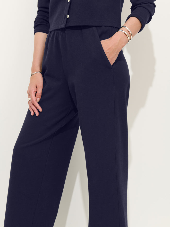 A person in a dark long-sleeve top and matching wide-leg Coco Sport Pant made from stretch cotton jersey, one hand in a pocket. Accessories include bracelets and rings; their face is unseen—an ideal women’s designer look.