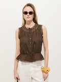 A woman in sunglasses wears the Collette Top In Ramie—a sleeveless brown vintage style with lace trim and a subtle peplum hem—paired with white pants. Her hair is loose, she sports a yellow scrunchie, all set against a plain light background.