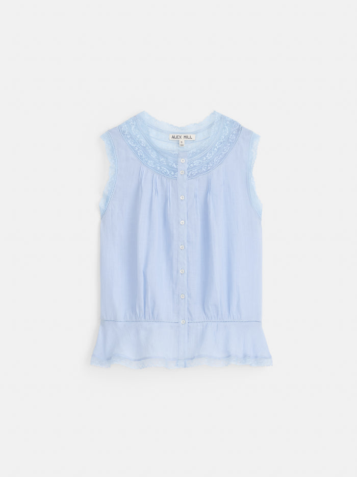 The Collette Top In Ramie is a sleeveless light blue vintage blouse with a round neckline, lace trim, front buttons, delicate embroidery at the collar and hem, and a soft feminine style finished with a ruffled peplum. Made from 100% ramie.