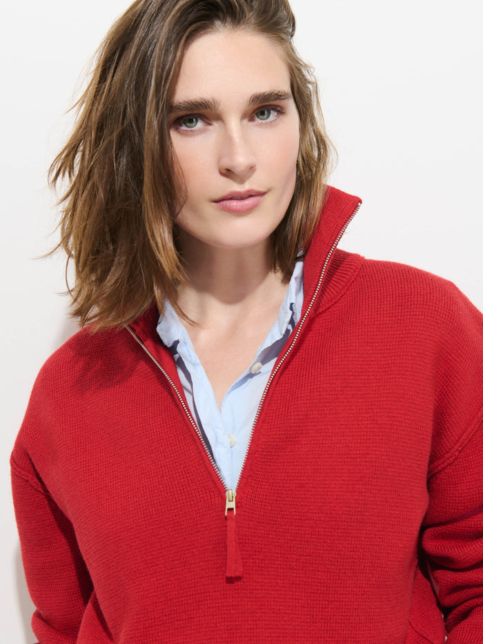 A person with shoulder-length brown hair wears the Daphne Half-Zip Sweater in Cotton Cashmere in red over a light blue collared shirt, standing against a white background and looking at the camera with a neutral expression.
