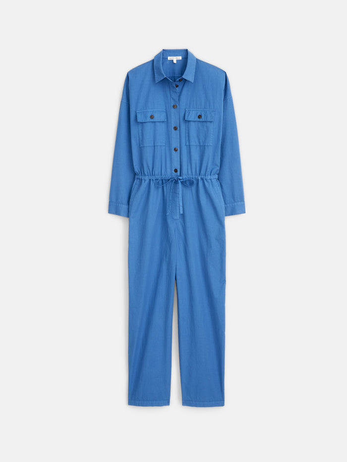 The Delancey Jumpsuit in Lightweight Twill is a women's blue cotton jumpsuit with a relaxed fit, long sleeves, collar, button-down front, chest pockets, and drawstring waist—shown laid flat on a white background.