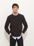 A young man with short brown hair stands against a white background, wearing the Donegal Crewneck Sweater over a light blue collared shirt, his hands in his pockets.