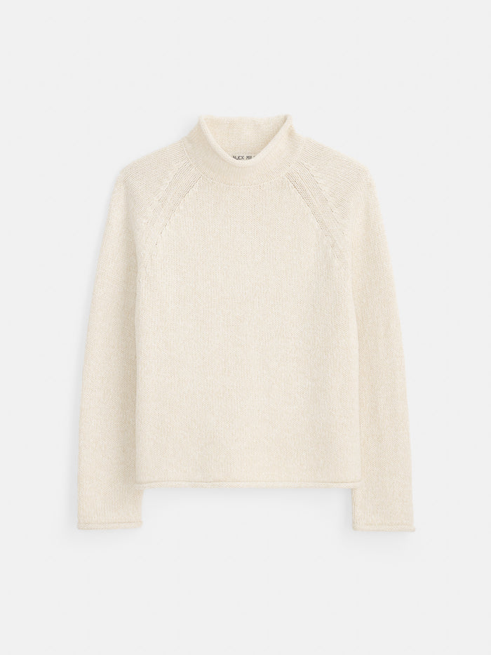 The Eastport Rollneck In Cotton is a cream-colored, long-sleeve knit sweater made from 100% cotton, featuring a mock neck and subtle textured detailing on the shoulders, shown against a plain white background.