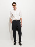 A man wearing a white button-up shirt, Flat Front Chino in Vintage Wash straight leg pants, a black belt, black shoes, and sunglasses stands against a plain white background.