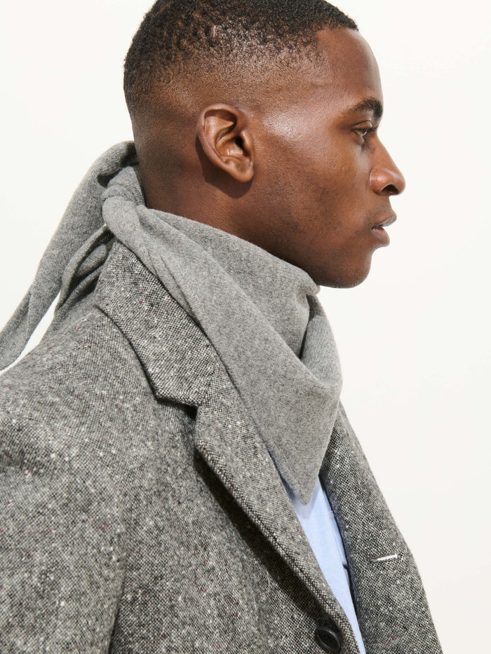 A man in profile wears the Handkerchief Scarf In Wool, wrapped snugly around his neck, paired with a textured gray coat against a simple light background.