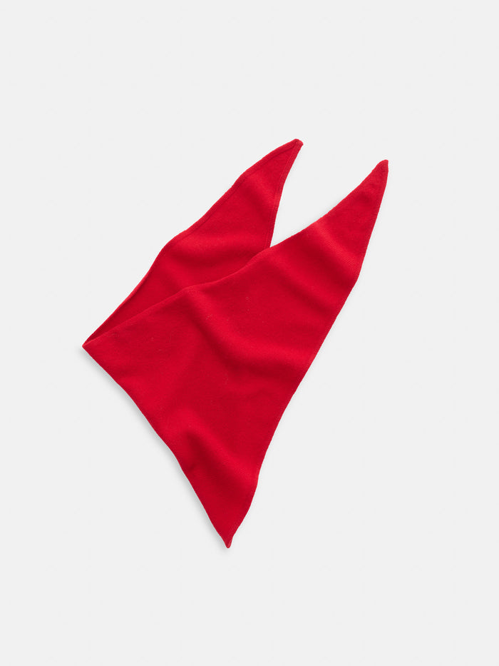 The Flynn Handkerchief Scarf in Wool, featuring a bright red triangular shape with two pointed ends, is laid flat on a white background.