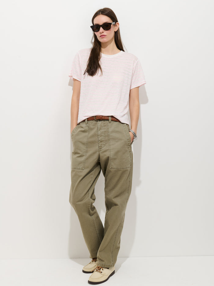 Woman wears the Garcon Striped Tee in linen cotton, olive cargo pants with front pockets, a brown belt, sunglasses, and beige sneakers, standing against a white wall with hands in her pockets—perfect for effortless year-round style.