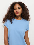 A woman with long, curly brown hair wears the Garcon Tee In Linen Cotton in light blue, standing against a plain white background and looking directly at the camera with a neutral expression.