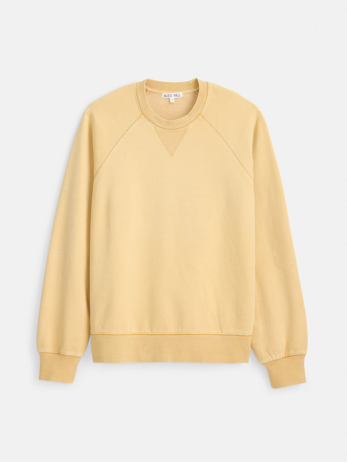 The Garment Dye Raglan Sweatshirt in Cotton Fleece is a light yellow crewneck sweatshirt crafted from 100% cotton fleece, featuring long sleeves, ribbed cuffs, and a ribbed hem. It is displayed on a white background.