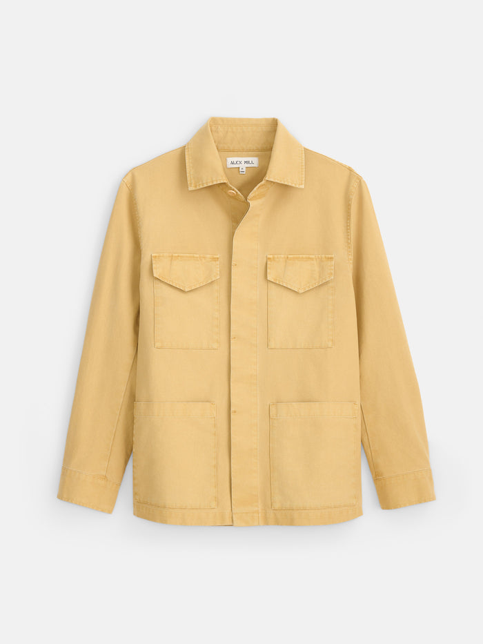 The Garment Dyed Chore Jacket in Canvas is presented against a plain white background. Crafted from garment-dyed canvas in light yellow, this utility jacket features a classic chore silhouette with a collar, button-down front, and four vintage hunting-inspired pockets—including two flap chest pockets and two lower patch pockets.