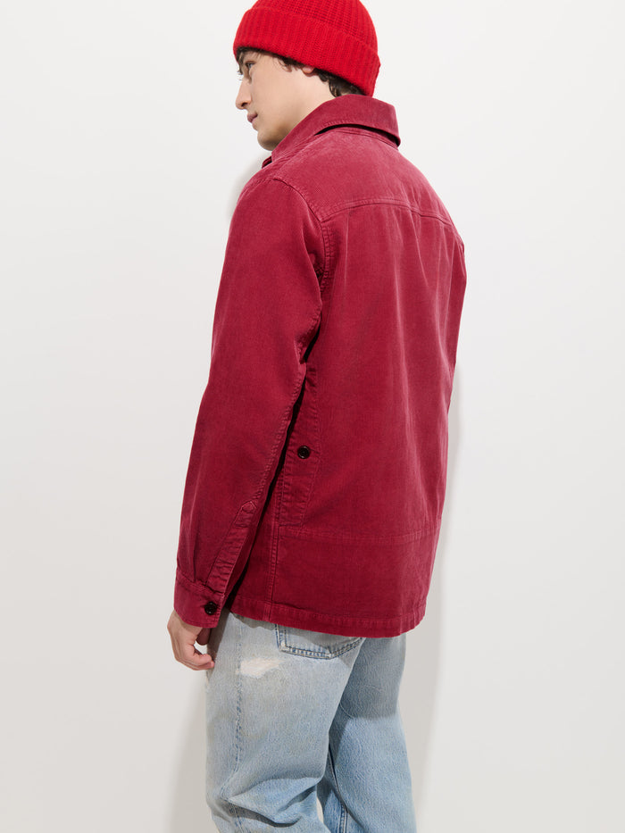 A person wearing the Garment Dyed Chore Jacket in Corduroy in red, styled with a matching red knit beanie and light blue jeans, stands facing away from the camera against a plain white background.