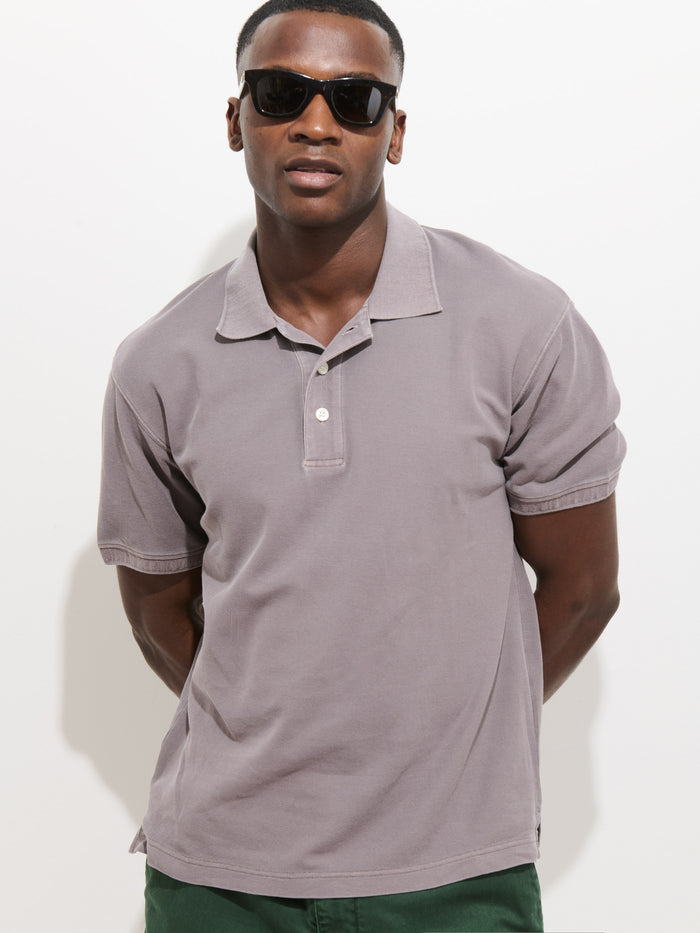 A man wearing dark sunglasses and a short-sleeved Garment Dyed Polo In Pique Cotton stands against a white background with his hands behind his back.