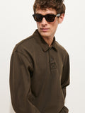 A man wearing dark sunglasses and a dark olive Garment Dyed Rugby Shirt In Cotton Jersey with a boxy fit looks to the side against a plain white background.