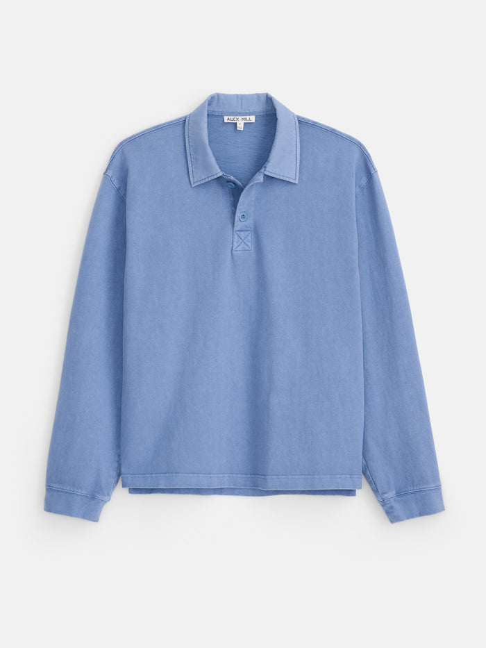 The Garment Dyed Rugby Shirt in Cotton Jersey is a light blue, long-sleeve shirt with a collar and three buttons at the top, featuring a relaxed boxy fit and shown on a plain white background.
