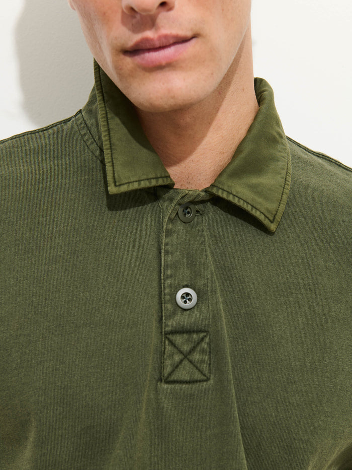 A person wearing the Garment Dyed Rugby Shirt In Cotton Jersey in olive green, featuring a collared neckline and two visible buttons, photographed from the shoulders up against a plain light background.
