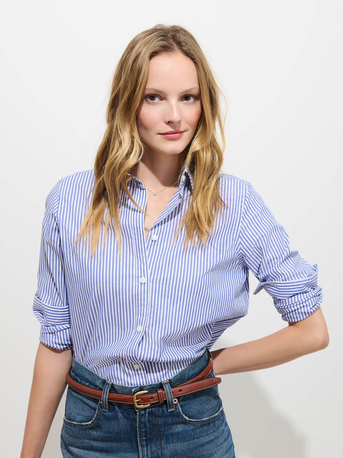 A woman with long blonde hair wearing the Gracie Striped Shirt in Poplin and jeans stands against a plain white background, posing with one hand on her hip and a slight smile.