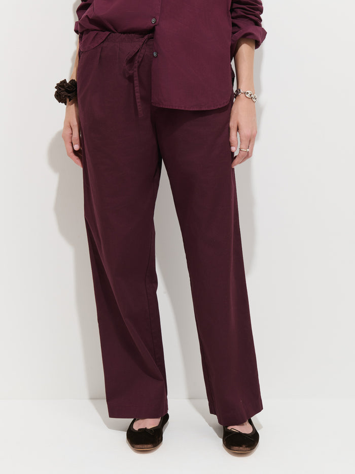 Wearing the Hudson Pant In Cotton Twill in burgundy—a wide-leg, loose-fit style—paired with a matching long-sleeve shirt, dark shoes, and a bracelet. The outfit is photographed from shoulders to feet against a plain background.