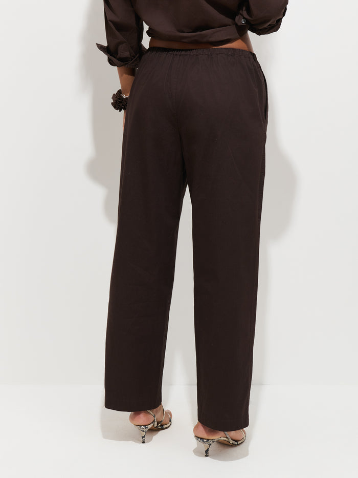 A person wearing the Hudson Pant in Cotton Twill—loose, black, wide-leg style—and heeled sandals, stands against a plain white background, shown from the back with hands resting at sides.