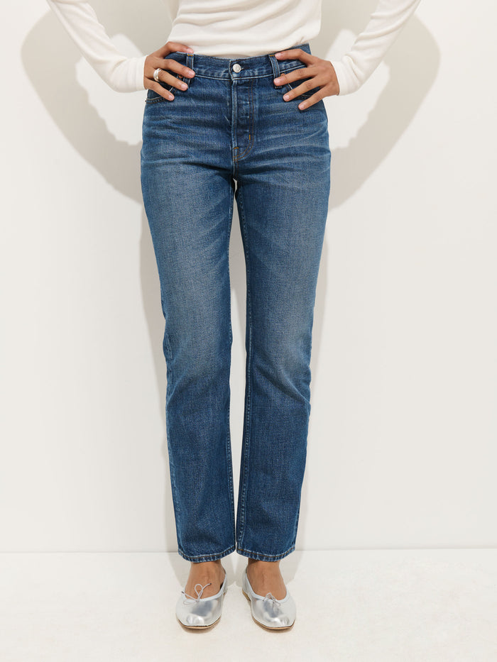 Wearing the Jane Mid Rise Straight Jean, a white long-sleeve top, and silver ballet flats, a person stands against a plain white background with hands on hips.