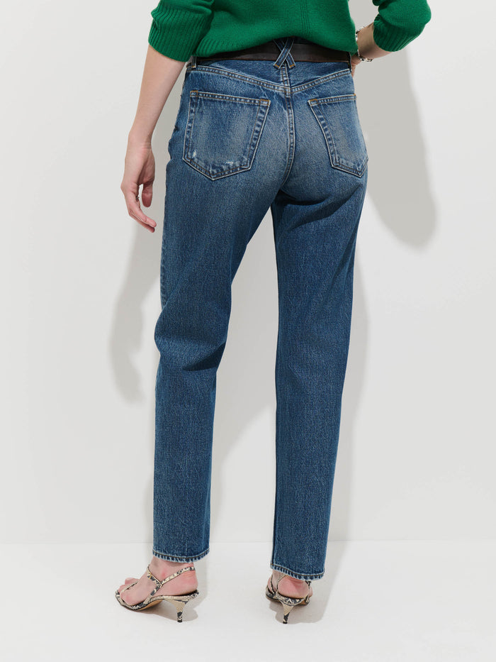 Wearing the Jane Mid-Rise Straight Jean, made from 100% cotton denim, styled with a green sweater and heeled sandals, this person stands with their back to the camera against a plain light background.