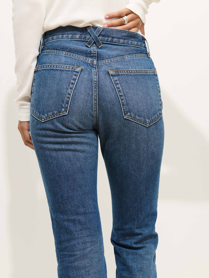 A person models the Jane Mid Rise Straight Jean, showing the back view with large pockets and crossed belt loops, paired with a white long-sleeve top.
