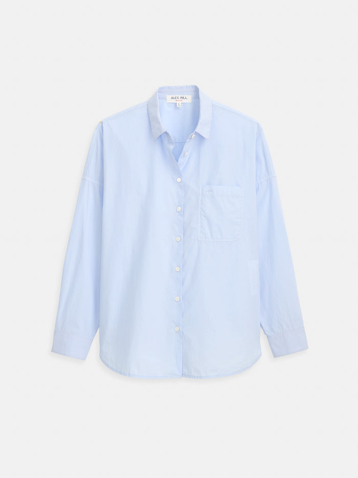 Jo Shirt in Cotton Poplin, shown in light blue, features an oversized fit, long sleeves, chest pocket, and is crafted from 100% cotton—presented laid flat on a white background.