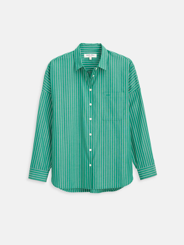 The Jo Striped Shirt In Cotton Poplin is a long-sleeve, button-up shirt made from 100% cotton poplin, featuring green and white vertical stripes, a collar, Troca shell buttons, and a front chest pocket, displayed against a plain light background.