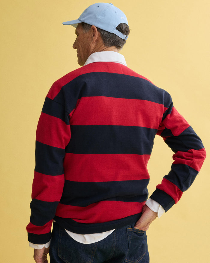 A person wearing a light blue baseball cap and the J.Press x Alex Mill Rugby Striped Shirt In Cotton stands facing away against a plain yellow background.