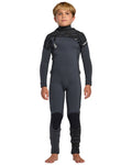 A young boy with short blond hair stands barefoot, wearing the Volcom Kids' 4/3 Modulator Chest Zip Full Wetsuit in dark gray with black patterned panels. He faces forward with arms relaxed at his sides.